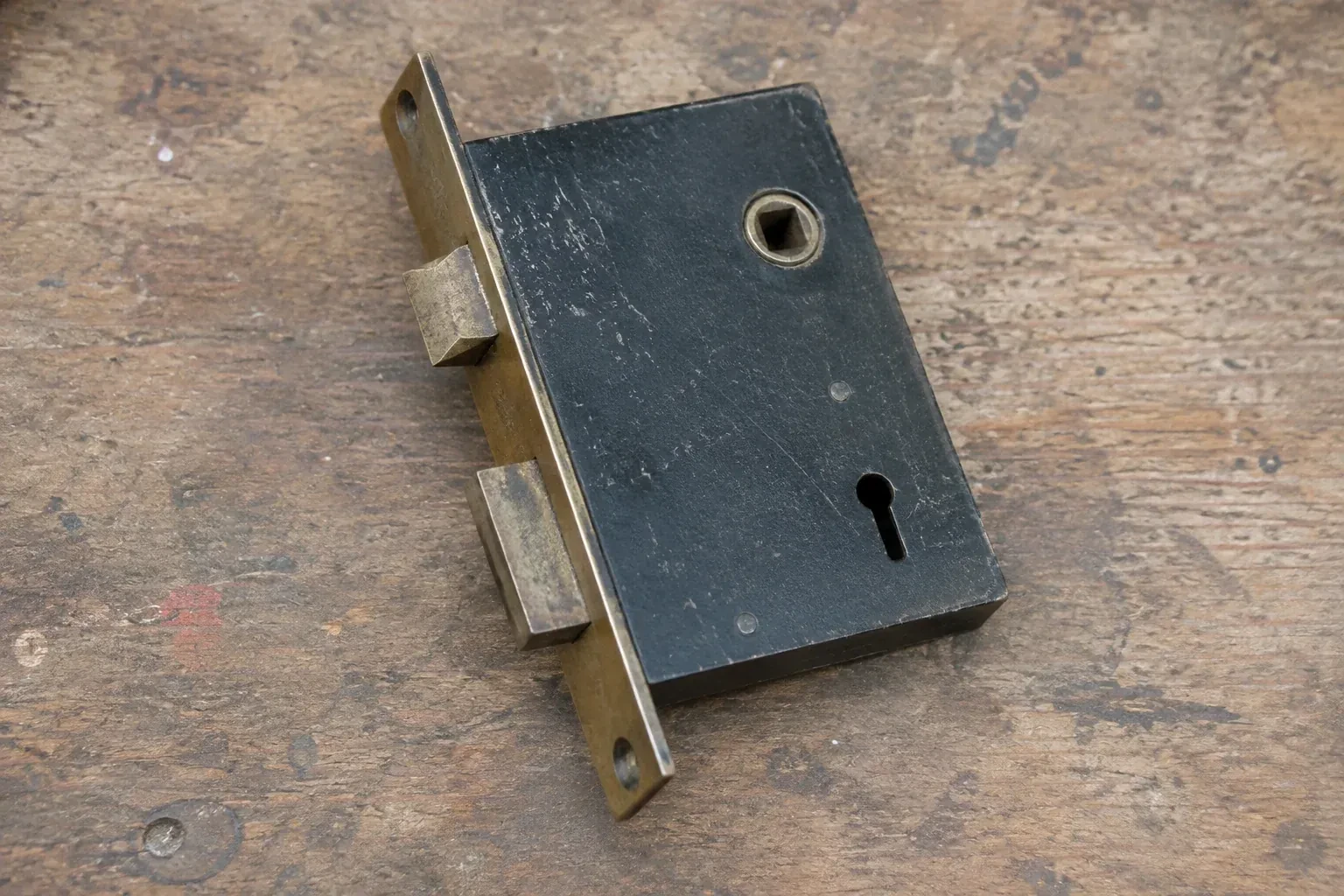 Closed mortise lock case with spindle opening, keyhole, latch and deadbolt on a wooden workbench. — Vintage Mortise Lock Service, Cambridge