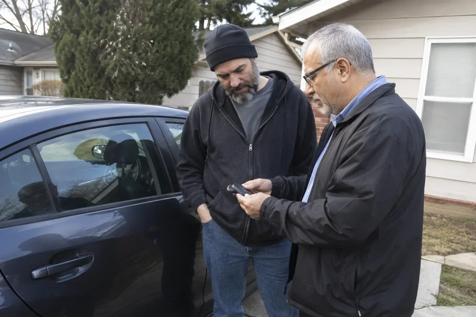 Two adults discussing a key fob beside a parked car. — Car Lockout Service, Cambridge